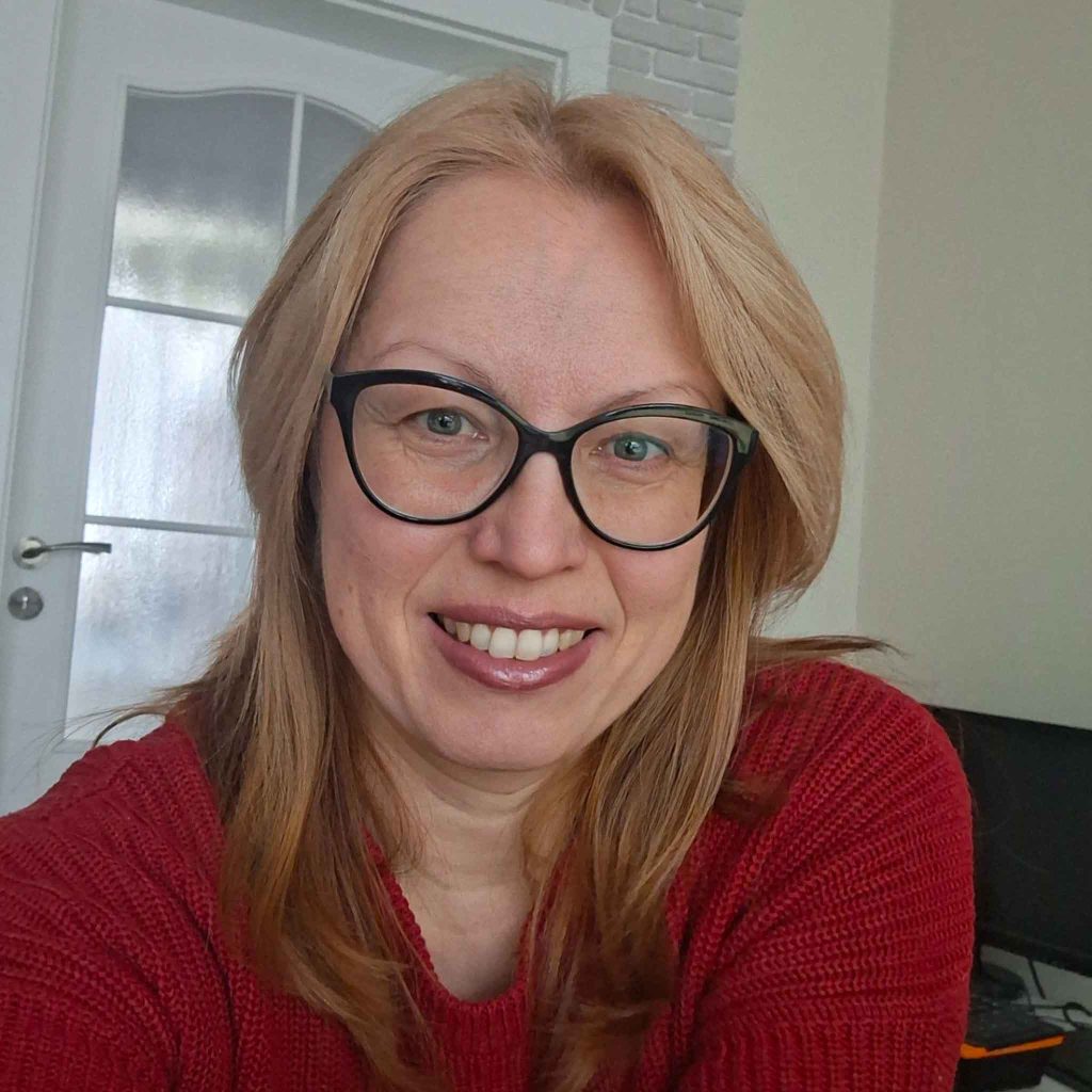 Portrait of Gergana, accountant at Aidos, smiling indoors, wearing glasses and a red sweater, professional headshot.